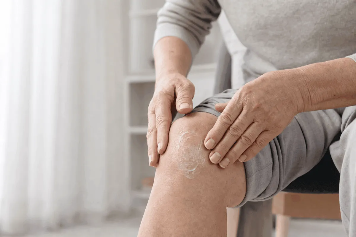 Personne assise, les deux mains posées sur son genou, une crème blanche étalée sur la rotule